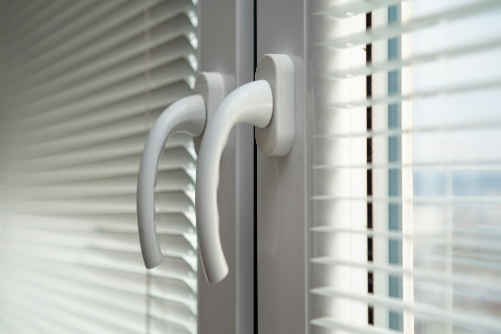 Handles of closed white plastic window with blinds